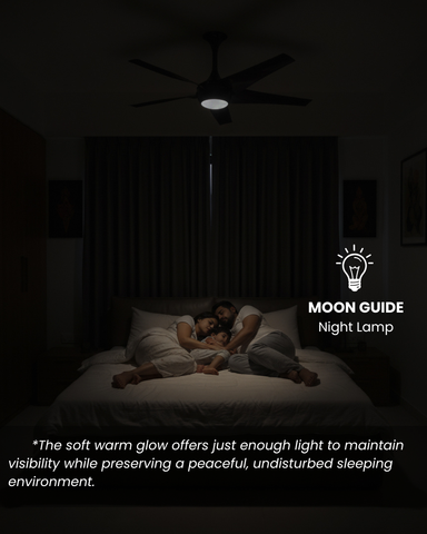 Family lying in bed under a Moon Guide night lamp in a dark bedroom.